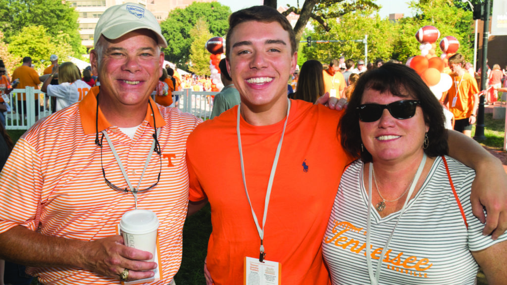 A student and his parents pictured in their Tennessee attire at a tailgate on campus before a football game.