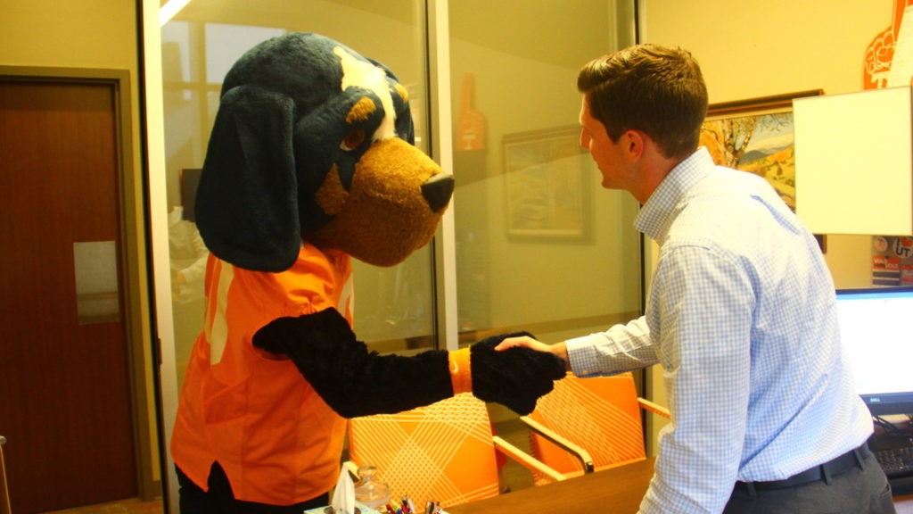 Smokey the mascot shaking hands with an employee inside of an office space.