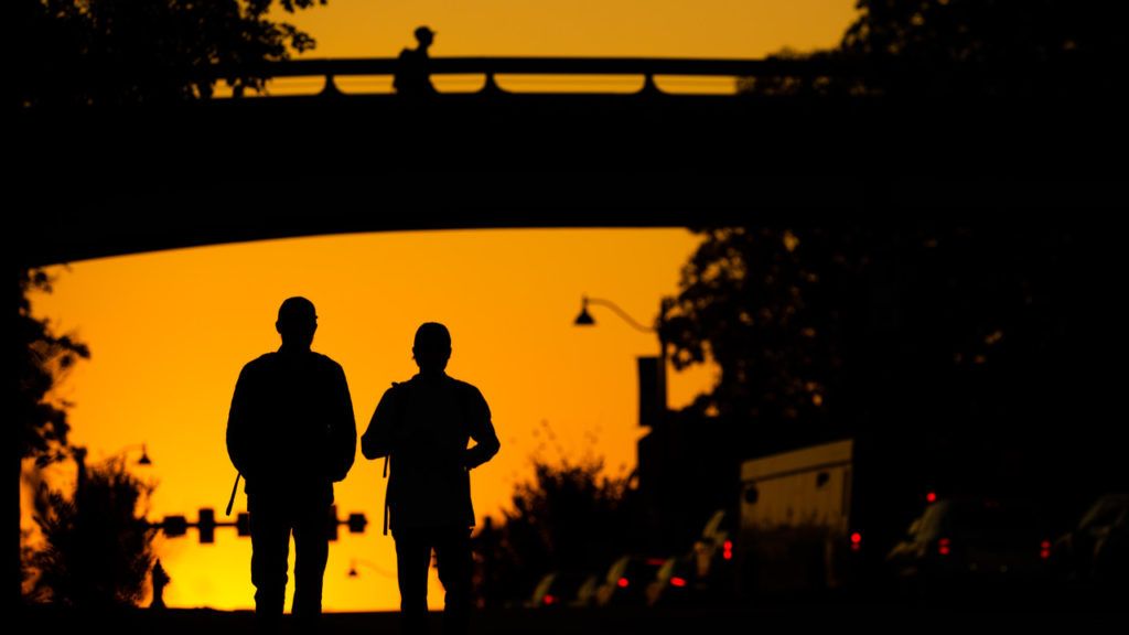 A picture of two students walking into the sunset under the pedestrian bridge on Cumberland Avenue.