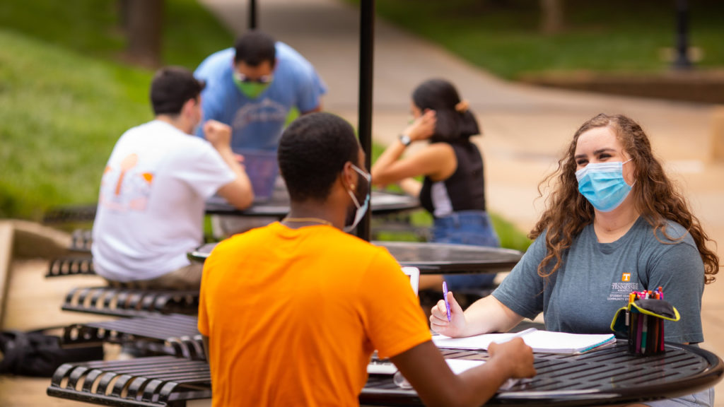 Two students talking at a picnic table on campus.